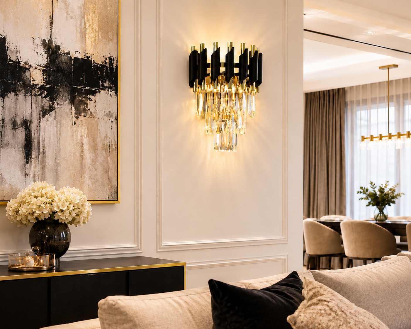 A modern wall sconce with a curved silver metal frame and cascading clear crystal droplets, illuminated with warm light on a beige wall above a marble console table.