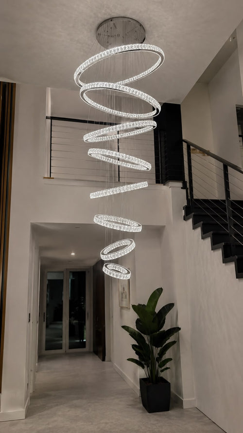 The Valora Crystal Chandelier elegantly suspended in a modern double-volume entrance, creating a breathtaking focal point with cascading crystal LED rings that illuminate the space with luxurious warmth and contemporary sophistication.