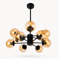 A modern multi-light chandelier with a matte black central hub and eight clear amber-tinted glass globes, shown against a plain light gray background.